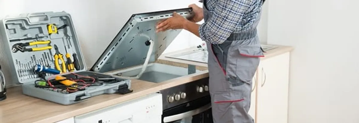 Cooktop repair technician lifting a built-in stovetop for service in Columbus, OH
